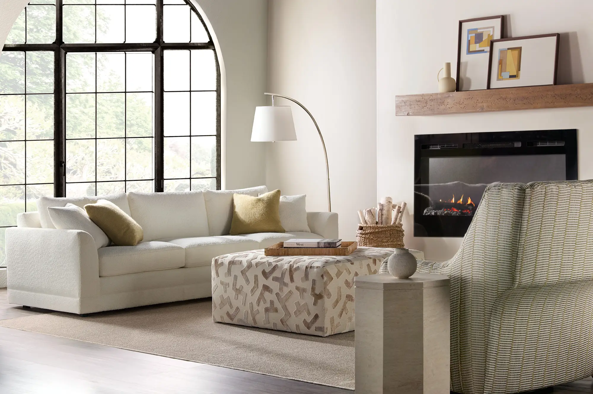 Living room with a cream sectional sofa, patterned ottoman and arched windows beside a lit fireplace