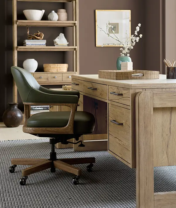 Home office with a light wood desk, green leather task chair and shelving