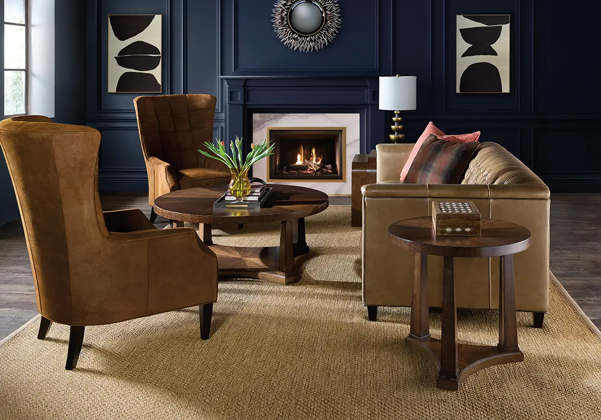 Navy panelled sitting room with leather wing chairs, round wood tables and a lit fireplace