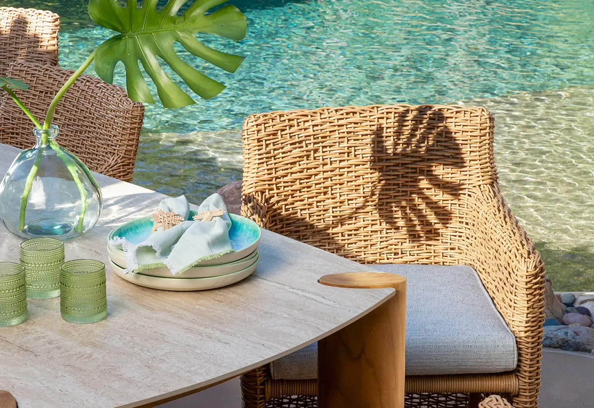 Woven outdoor armchairs and a table set with glassware beside a turquoise pool