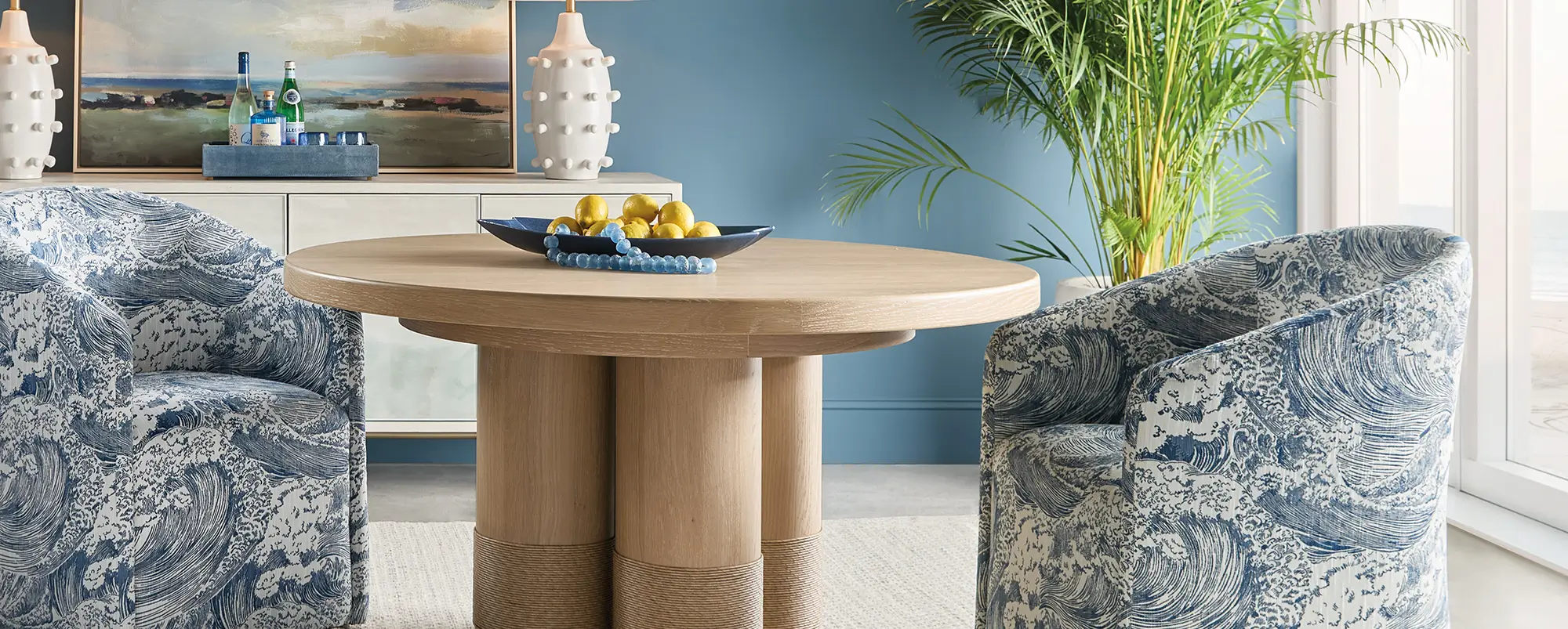 Round oak dining table and patterned armchairs against a deep blue wall