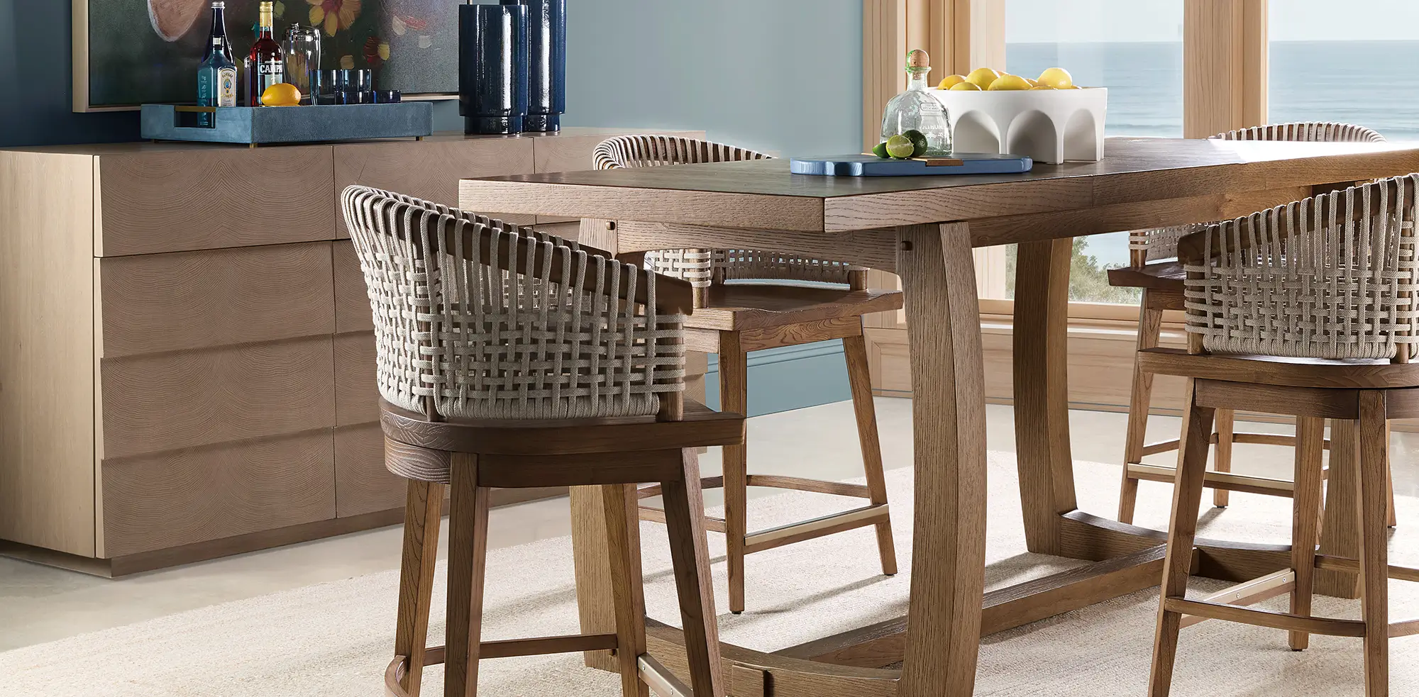 Woven counter stools at a light oak island with an ocean view beyond