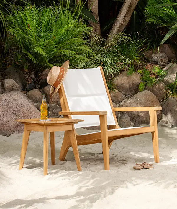 Teak and canvas outdoor lounge chair on a sandy shoreline